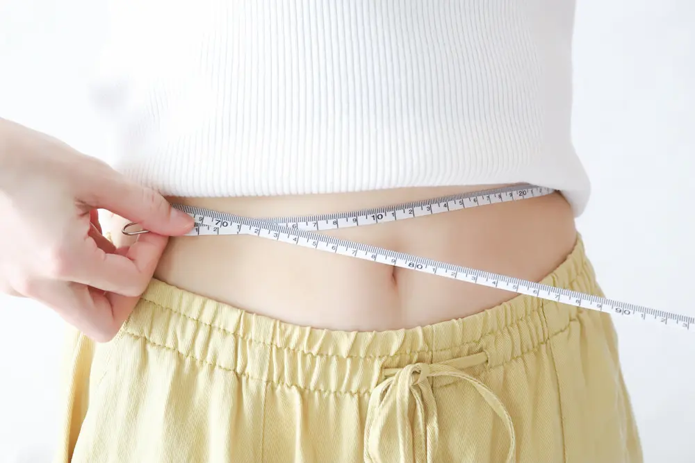 お腹周りをメジャーで測定する女性の画像